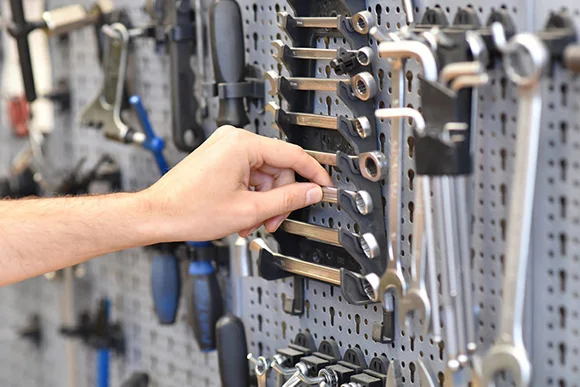 Eine Hand greift nach einem Schraubenschlüssel an einer Werkzeugwand.